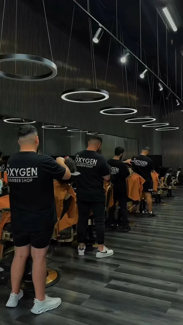 Four barbers in Oxygen tees working clients beneath the neon chandelier