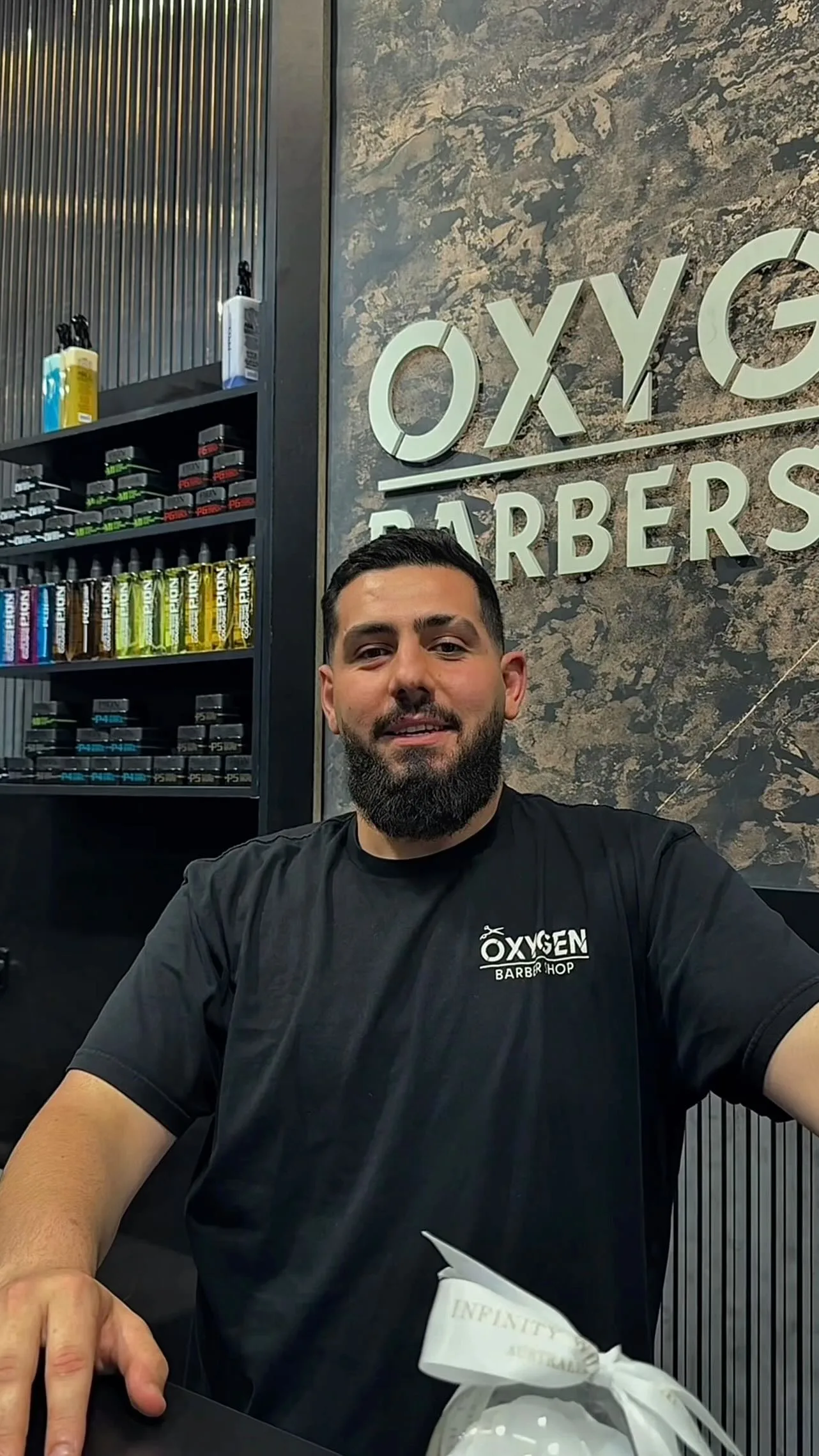 Barber in Oxygen tee beside the product wall
